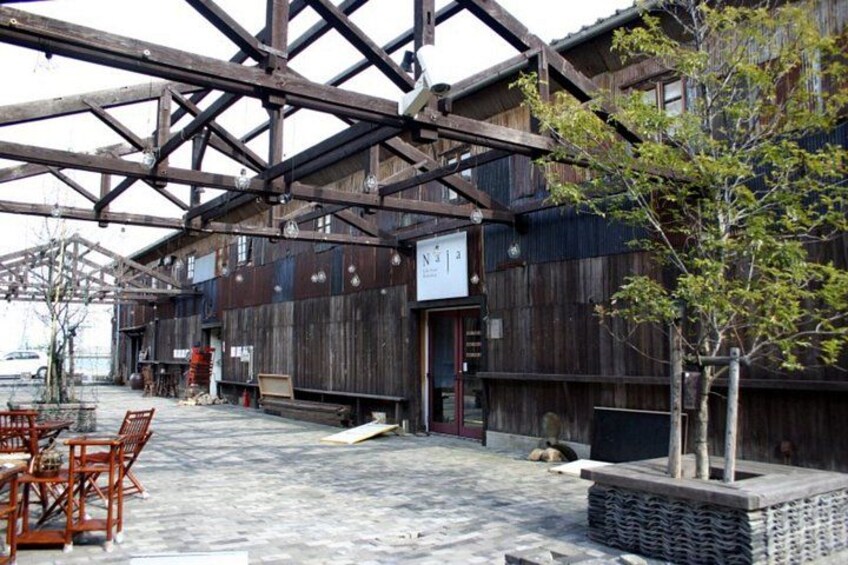 A rustic wooden building with a metal roof structure, outdoor seating, and a small tree. 3