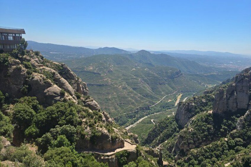 A mountainous landscape with a building on a cliff, a valley, and a winding road. 2
