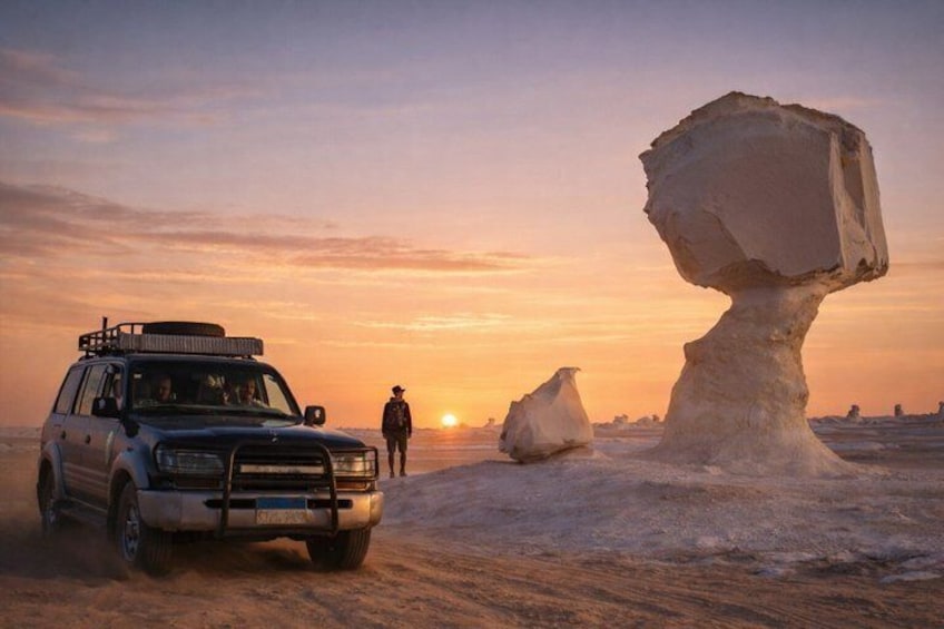 A desert landscape with a large rock formation, a vehicle, and a person walking. 1