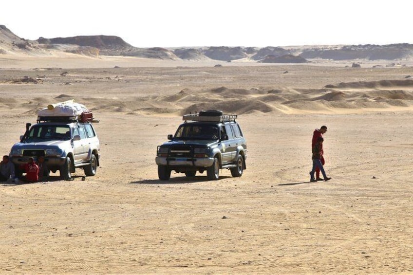 Two vehicles in a desert with a person walking between them. 3