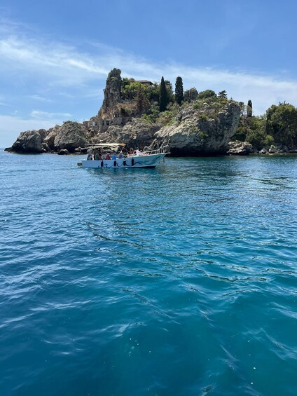 A boat with passengers on a clear blue sea, rocky coastline with vegetation, and a prominent cliff structure. 5