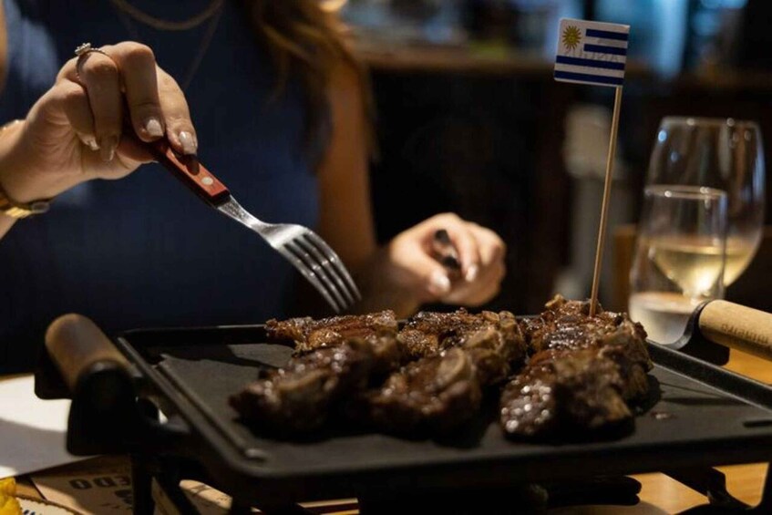 A person holding a fork with a flag, eating grilled meat on a plate. 3