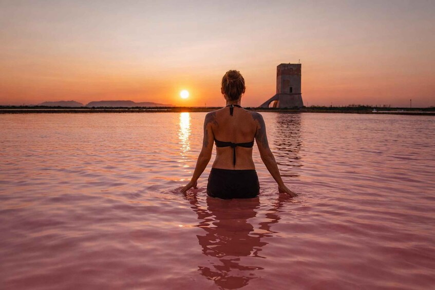 A person standing in water facing a sunset with a tower in the background. 3