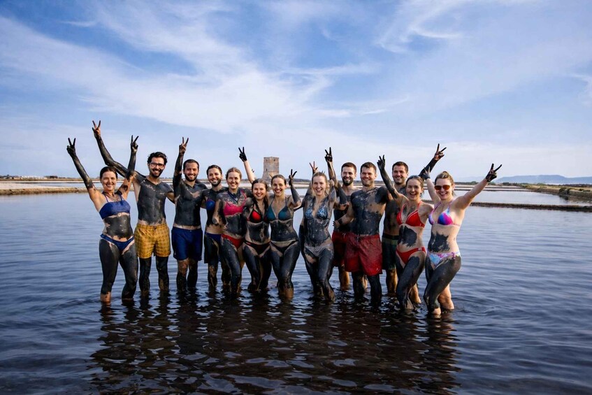 A group of people standing in water with their arms raised, wearing swimsuits and mud-covered. 1