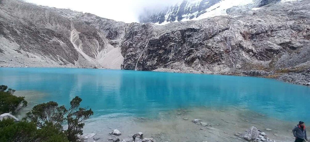 A turquoise lake surrounded by rocky mountains with sparse vegetation. 1