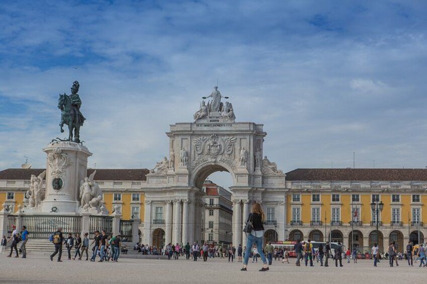A historic archway with statues, surrounded by a plaza with people and buildings. 2