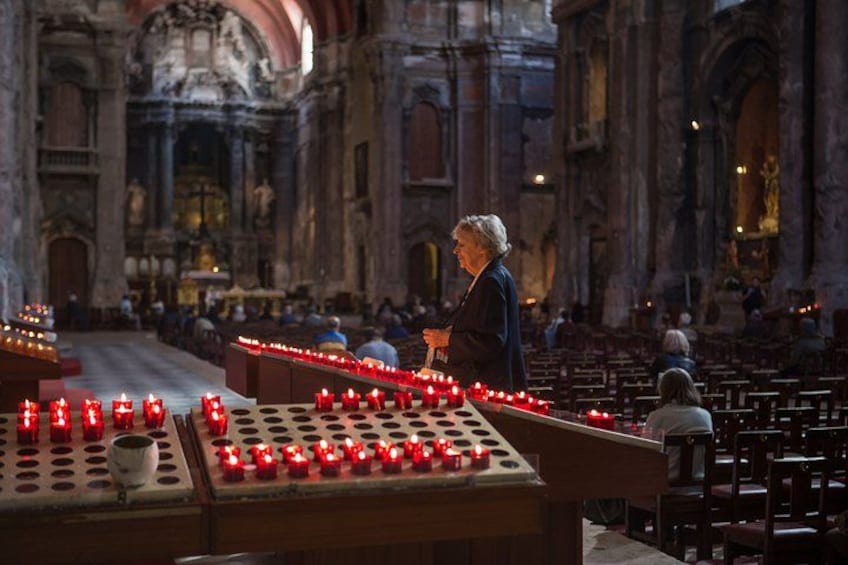 A church interior with rows of pews, a central aisle, and a woman standing near a table with lit candles. 3