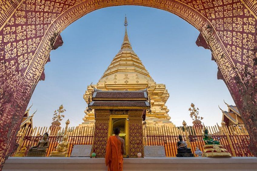 Un stupa doré orné de motifs complexes, une arche et une personne vêtue d’une robe orange. 1