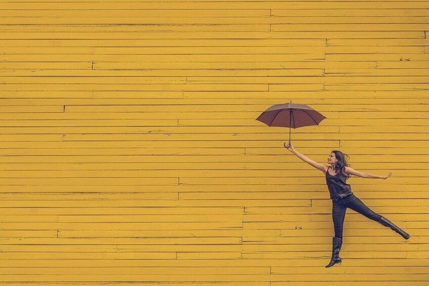 A person with an umbrella against a yellow wooden wall. 4