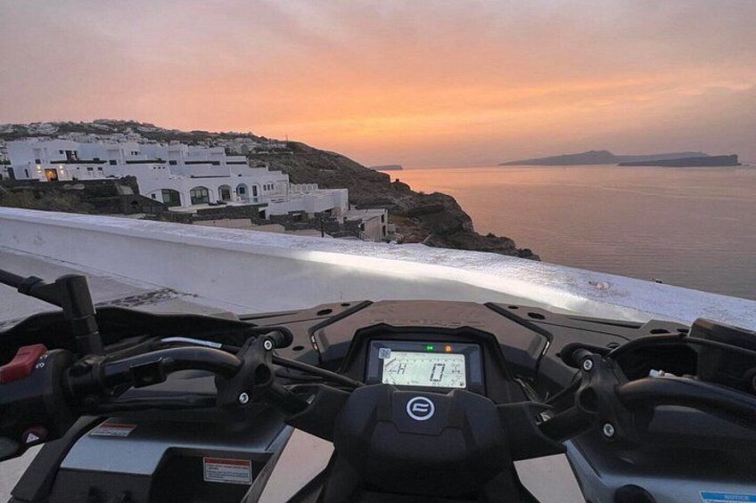A motorcycle's dashboard with a digital display, a coastal landscape with white buildings, and a sunset over the sea. 4