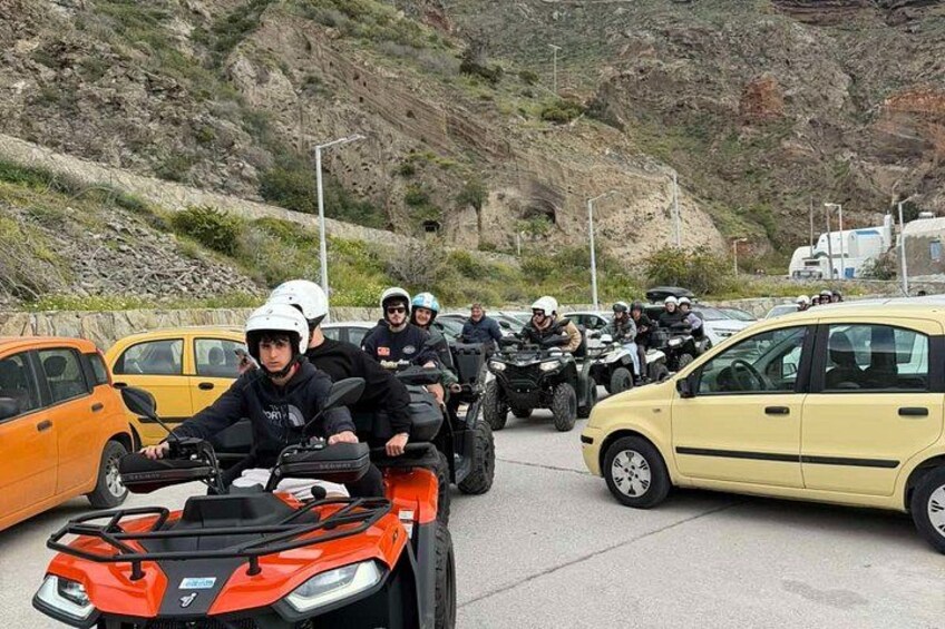 A group of people on ATVs in a parking lot with cars and a rocky hillside in the background. 2