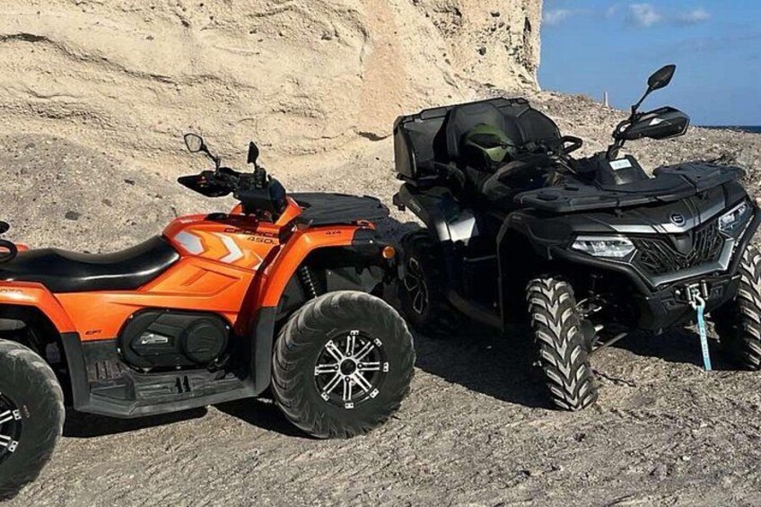 Two ATVs parked on a rocky terrain with a cliff in the background. 1