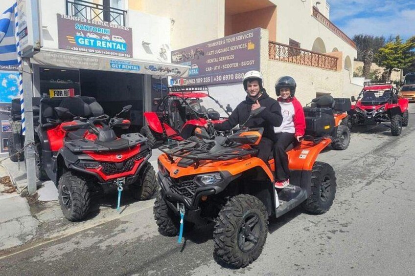 Two people on orange ATVs parked in front of a rental service building. 3