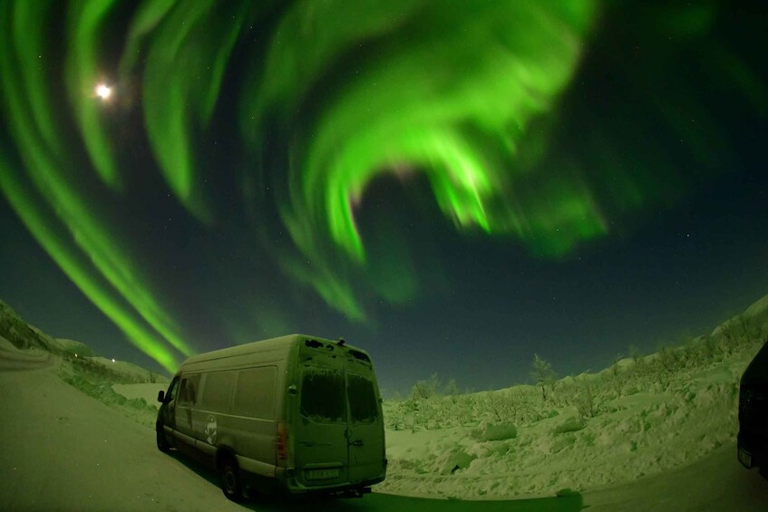 A van parked on a snowy road with the aurora borealis in the background. 3