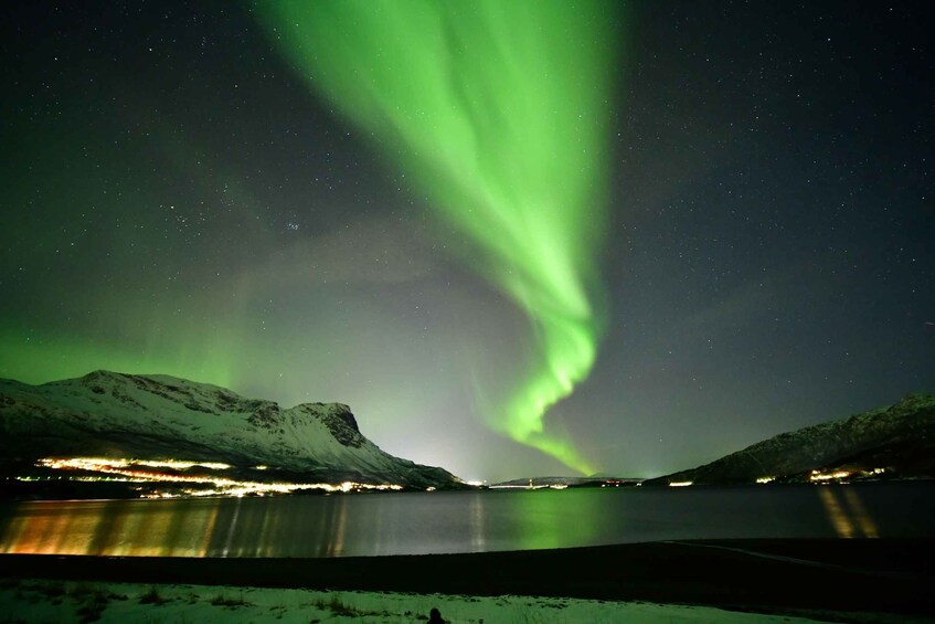 The Northern Lights over a snowy landscape with a lake and distant lights. 2