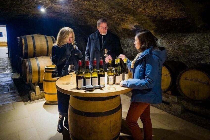 A group of people in a wine cellar with barrels and bottles of wine. 1