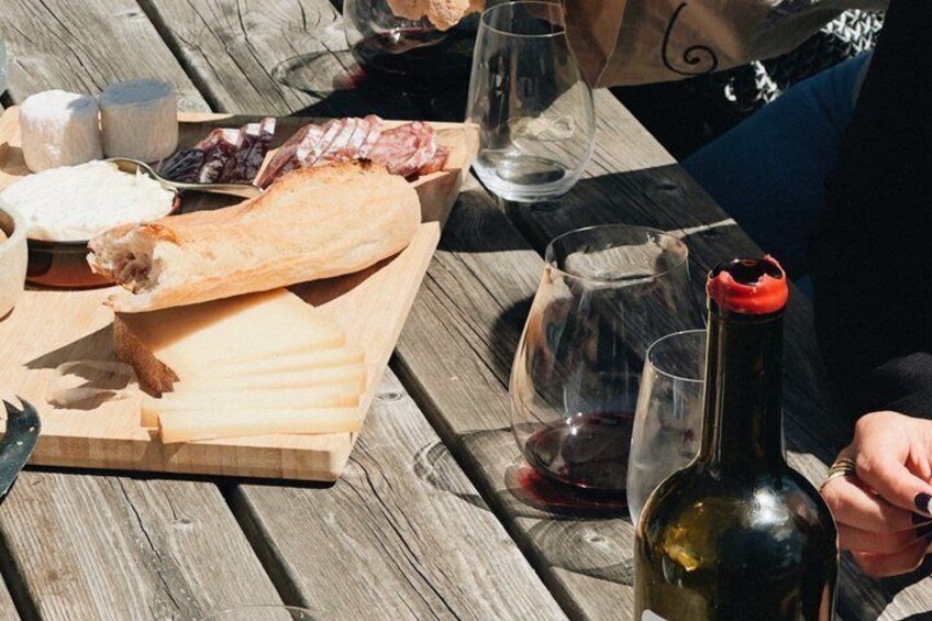 A wooden table with a charcuterie board, wine glasses, and a bottle of red wine. 3