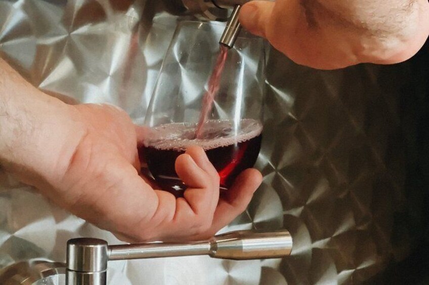 A person pouring red liquid from a tap into a glass. 2