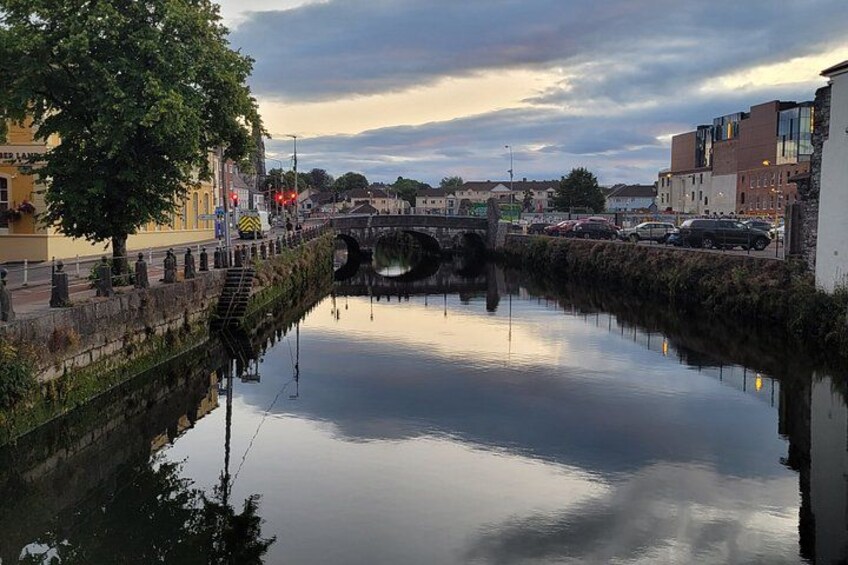 A calm river with a bridge, buildings, and a tree reflecting in the water. 2
