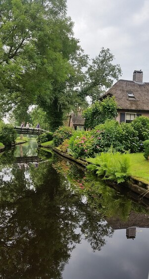 A calm pond with a bridge, lush greenery, and a traditional house with a thatched roof. 5