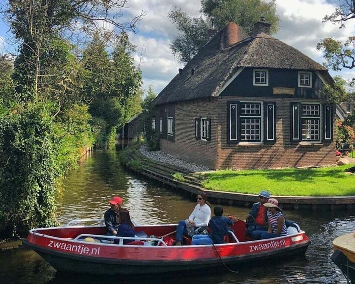 A narrow canal with a traditional house on the right and a red boat with passengers. 1