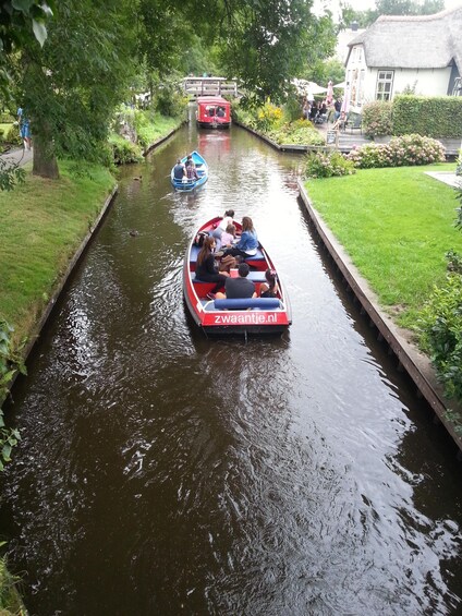 A narrow canal with boats, greenery, and a bridge. 3