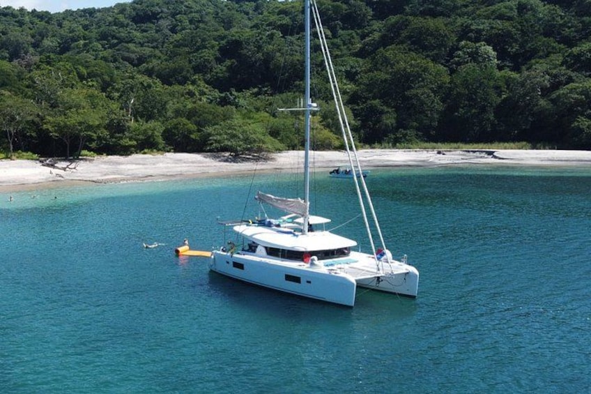 Una barca a vela bianca ancorata vicino a una spiaggia sabbiosa, con una fitta vegetazione sullo sfondo. 1
