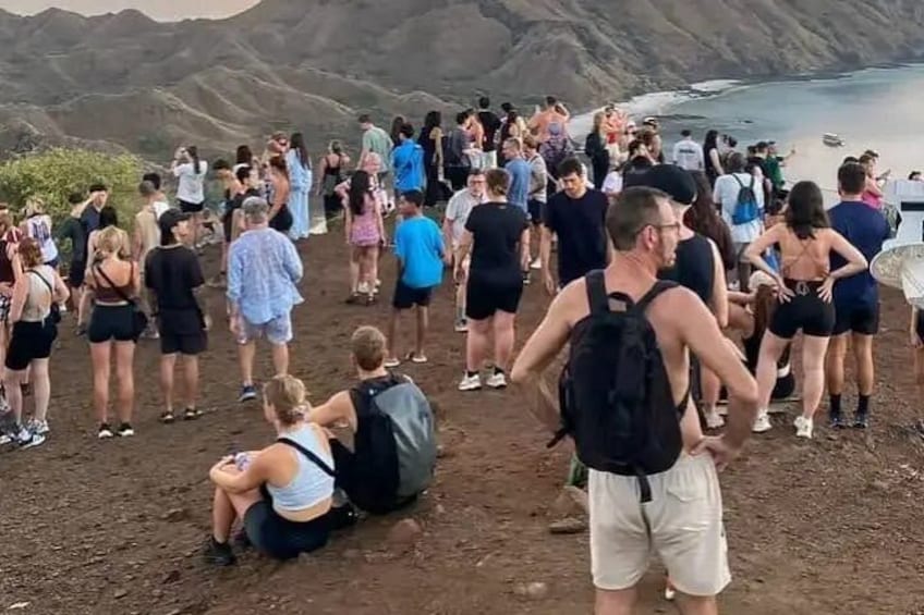 A group of people standing on a dirt path overlooking a body of water with hills in the background. 4