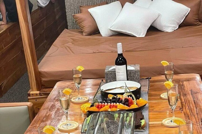 Spisebord med vinflaske, glas og en frugtfat i et hyggeligt rum med en seng i baggrunden. 2