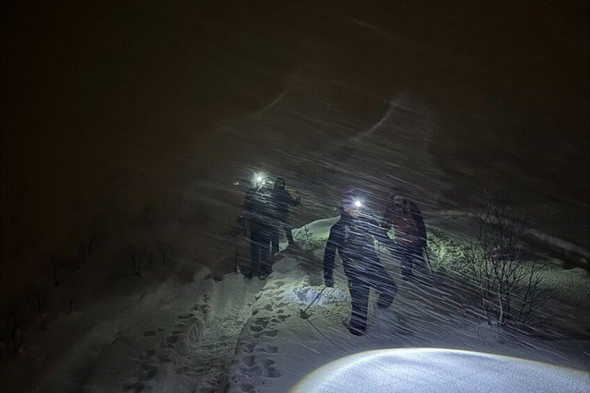 Twee personen lopen 's nachts met zaklantaarns door een besneeuwd landschap. 5