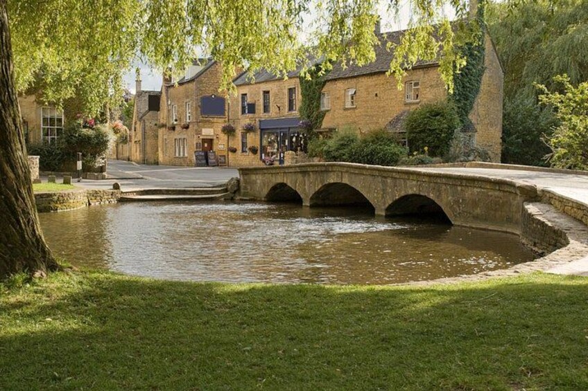 A stone bridge over a canal, surrounded by buildings with ivy and hanging flower baskets. 4