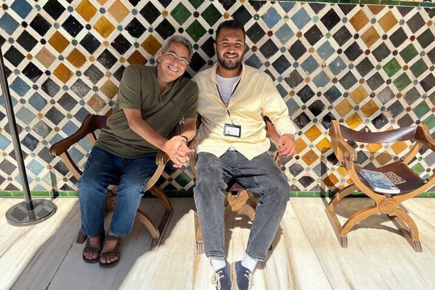 Deux personnes assises sur des chaises en bois, avec un mur à motifs en arrière-plan. 4