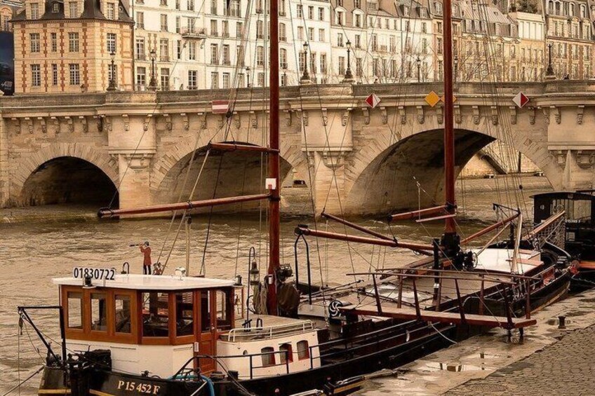 Une rivière où sont amarrés des bateaux, un pont de pierre et des bâtiments en arrière-plan. 2
