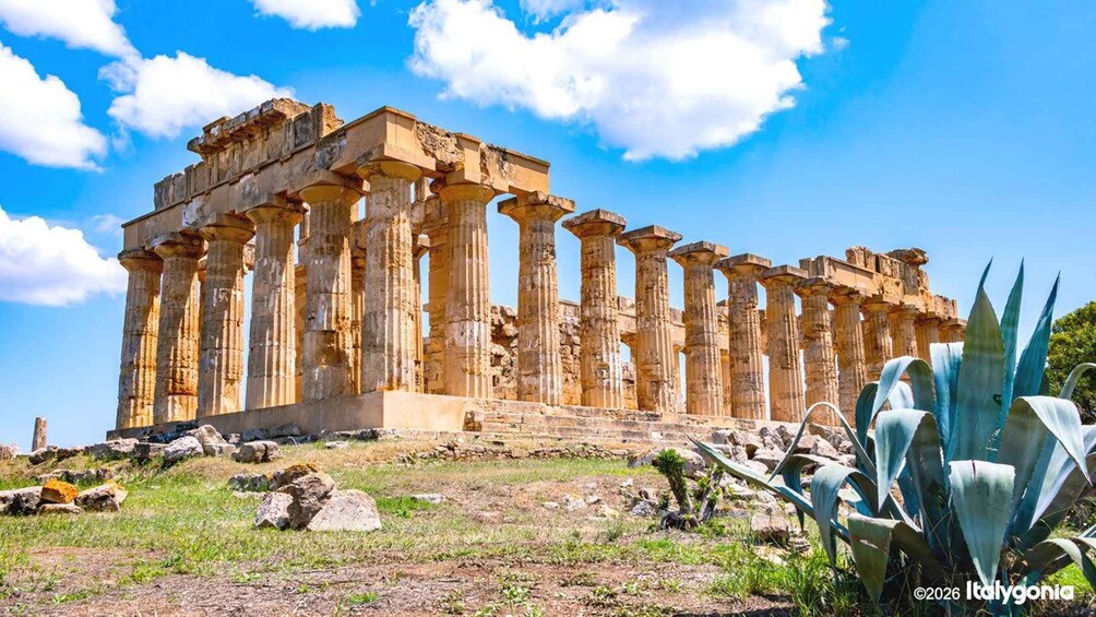 An ancient Greek temple with columns and ruins on a grassy hill. 1