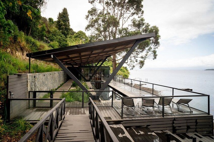 A wooden deck with a metal railing, a covered seating area, and a view of the water. 2