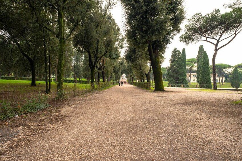 A gravel path flanked by trees in a park with a distant building. 5