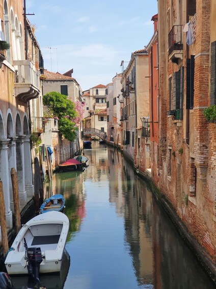 A narrow canal flanked by historic buildings, a small boat docked on the left, and a bridge in the distance. 2