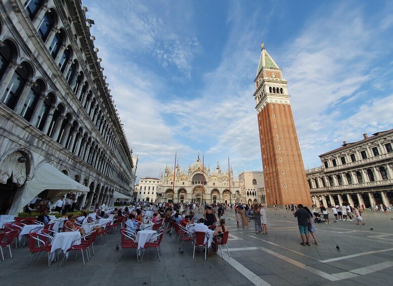 A piazza with outdoor seating, a prominent tower, and ornate buildings in the background. 5