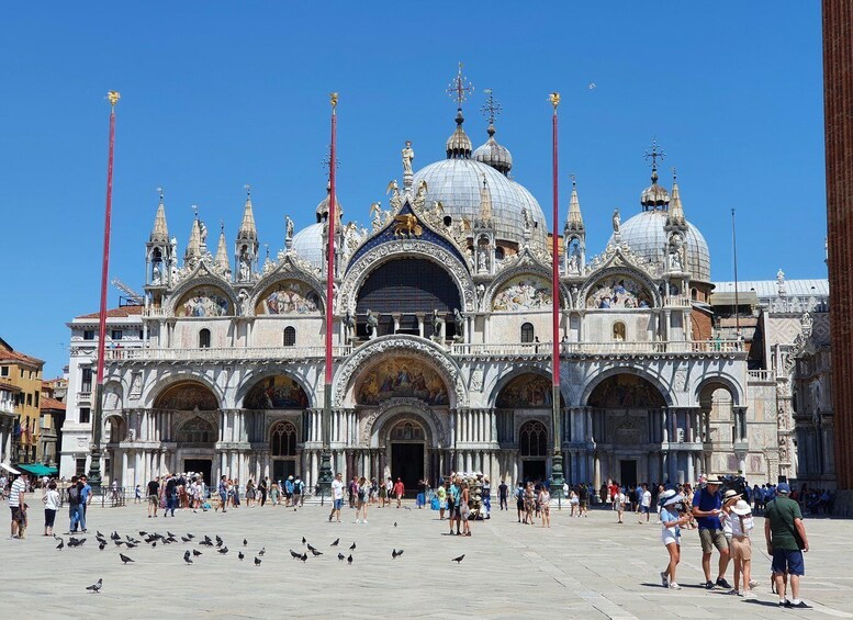 A historic cathedral with ornate architecture, including multiple domes and statues, and a plaza with people and pigeons. 1