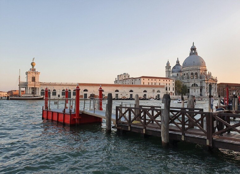 A waterfront with a wooden pier, a large white building with a dome, and a smaller tower with a statue. 3