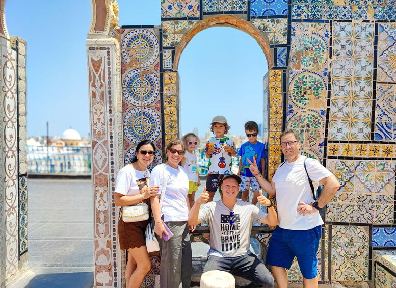 A group of people posing in front of a colorful tiled archway with intricate patterns. 2