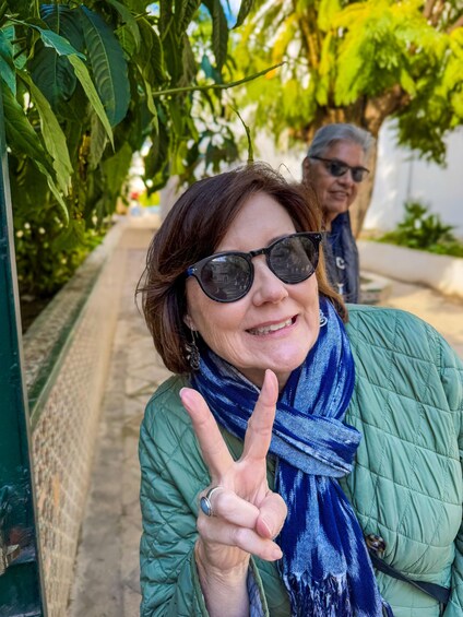 A person in a green jacket and blue scarf making a peace sign. 3