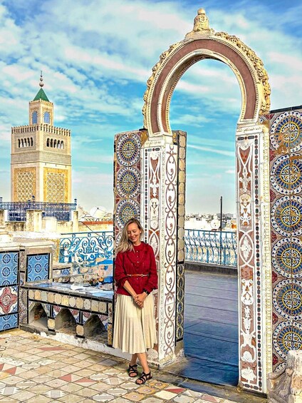 A person standing in front of a decorative archway with intricate tile work, overlooking a cityscape with a prominent tower. 1