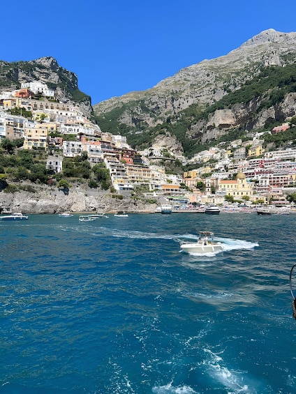 A coastal town with colorful buildings on a hillside, boats on the water, and mountains in the background. 1