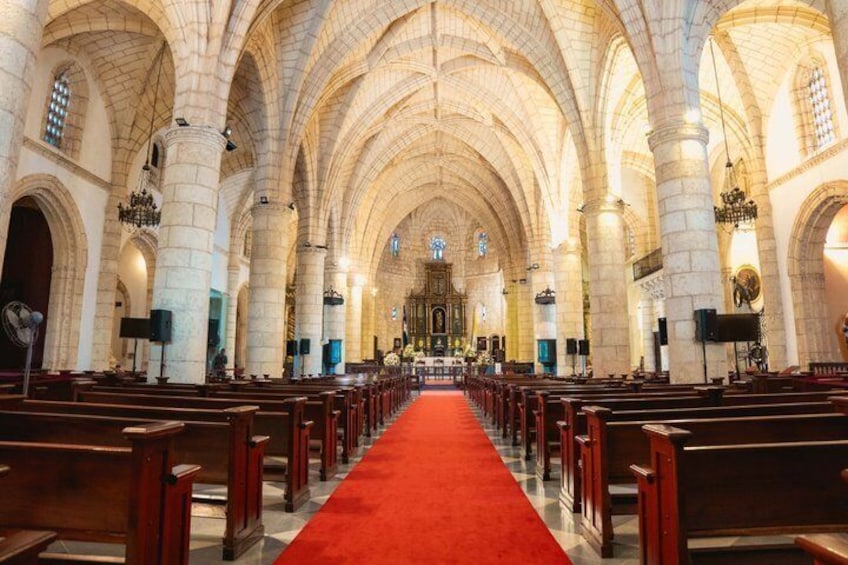 En interiörbild av en katedral med välvda tak, kyrkbänkar och en röd matta som leder fram till altaret. 4
