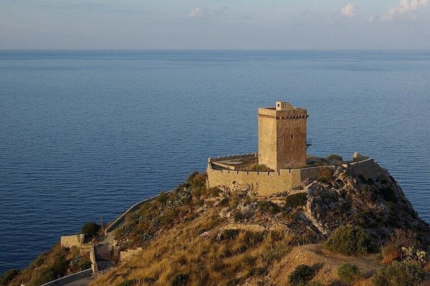 A coastal fortification with a prominent tower, surrounded by rugged terrain and overlooking the sea. 2