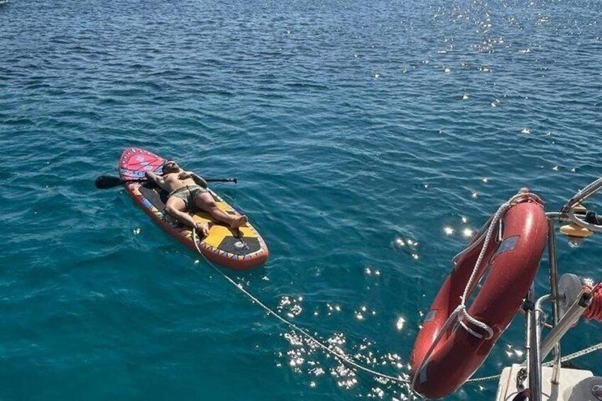 A person lying on a paddleboard in the water, a red life preserver, and a boat. 5