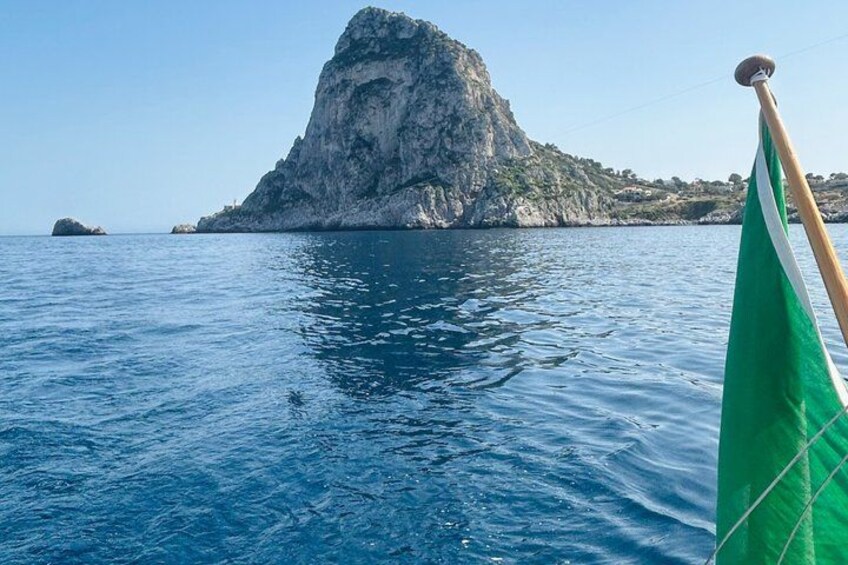A boat with a green flag, calm blue sea, and a rocky island in the background. 4