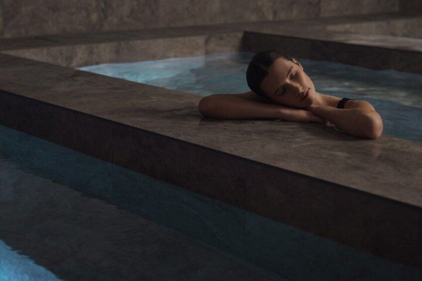 A person resting on a stone ledge by a pool. 4