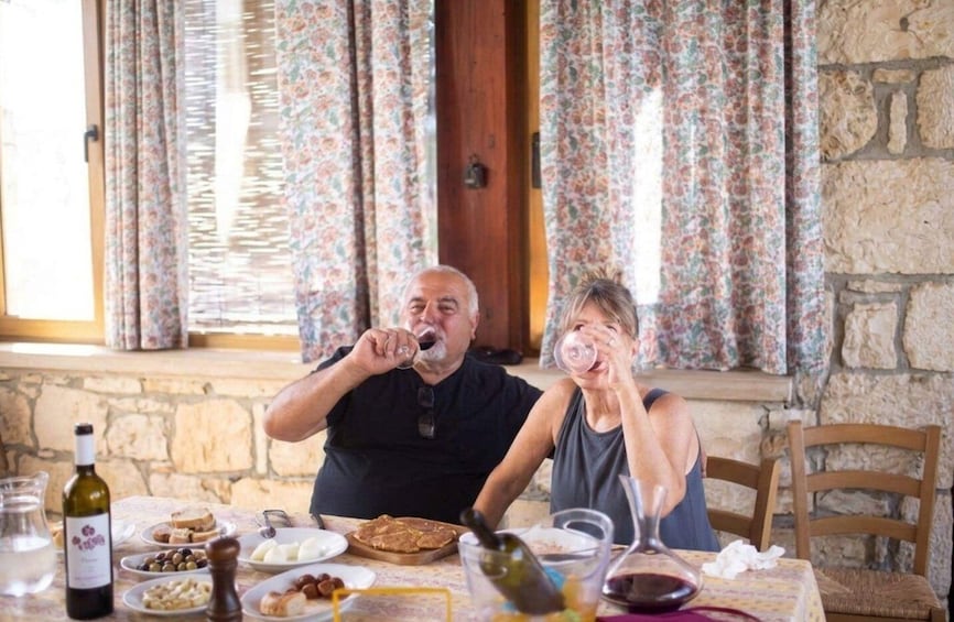 Two people sitting at a table with food and drinks, in a room with floral curtains and stone walls. 2